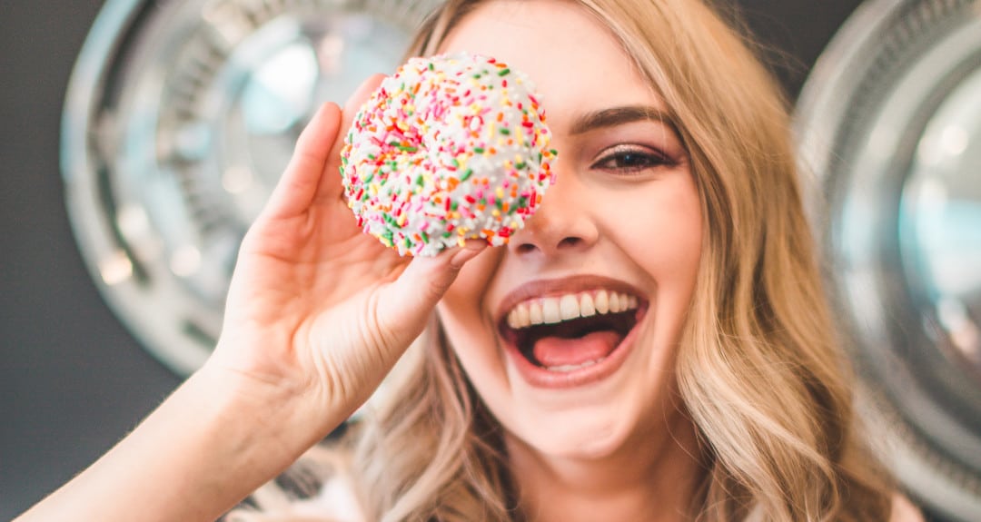 woman laughing and holding a sprinkled doughnut