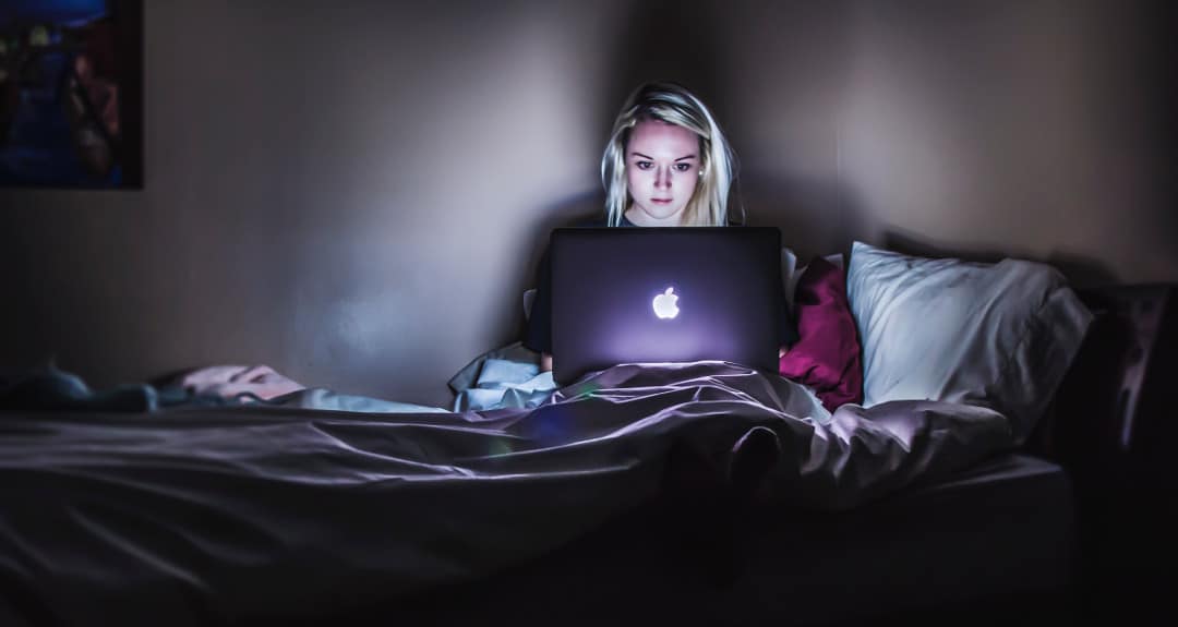 young woman using her laptop in bed to look for the best weight loss affiliate programs