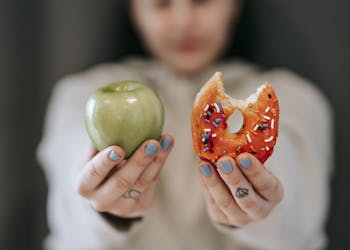 A close-up of a person holding an apple and a donut, symbolizing the choice between healthy eating and indulgence.