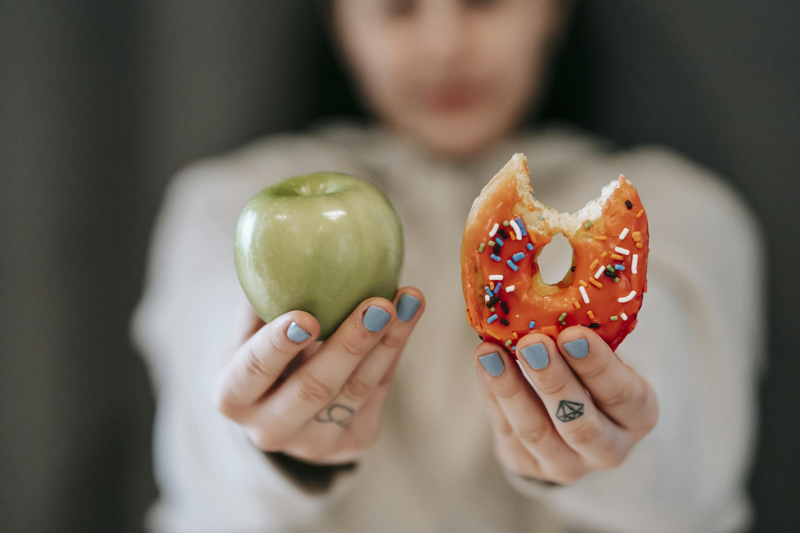 A close-up of a person holding an apple and a donut, symbolizing the choice between healthy eating and indulgence.