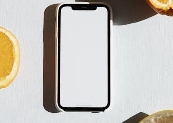 A smartphone surrounded by citrus fruit slices on a bright surface with dramatic shadows.