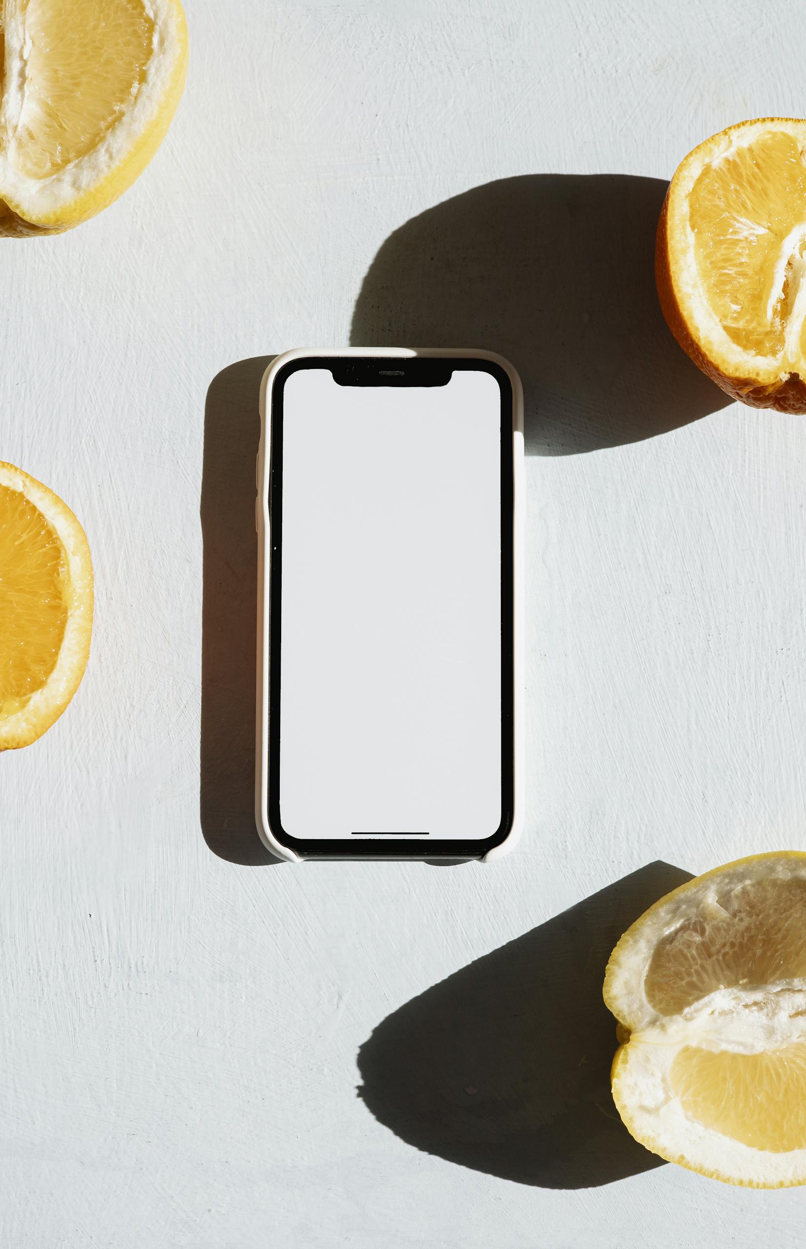 A smartphone surrounded by citrus fruit slices on a bright surface with dramatic shadows.