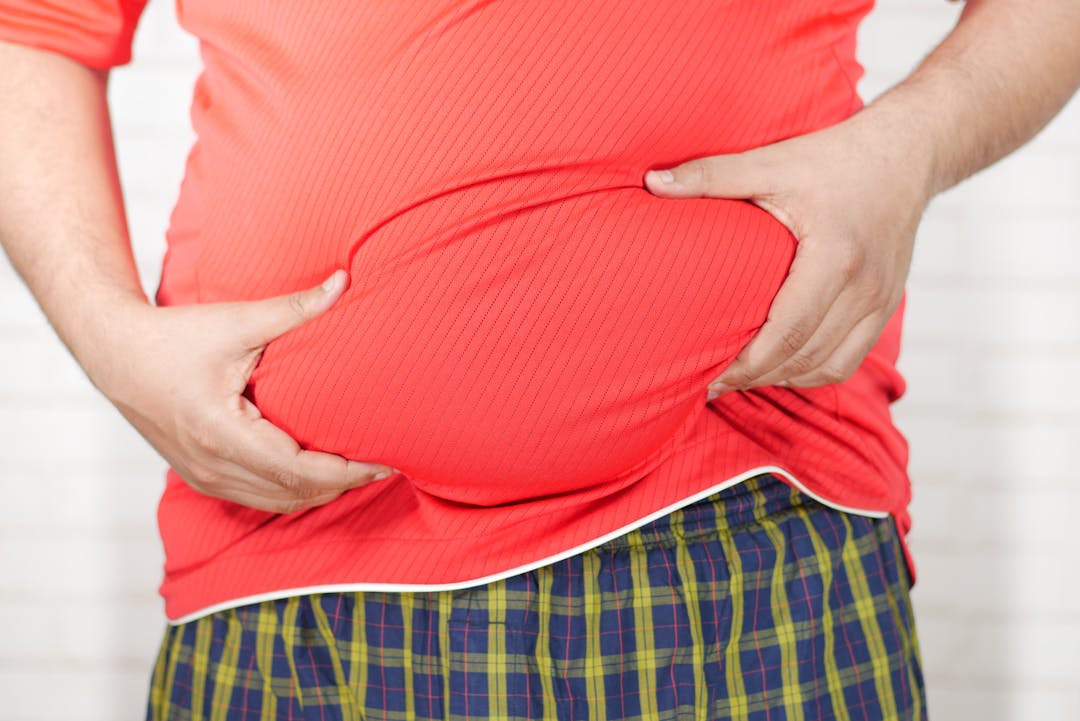 Close-up image of a man holding his bloated belly while wearing a red shirt.