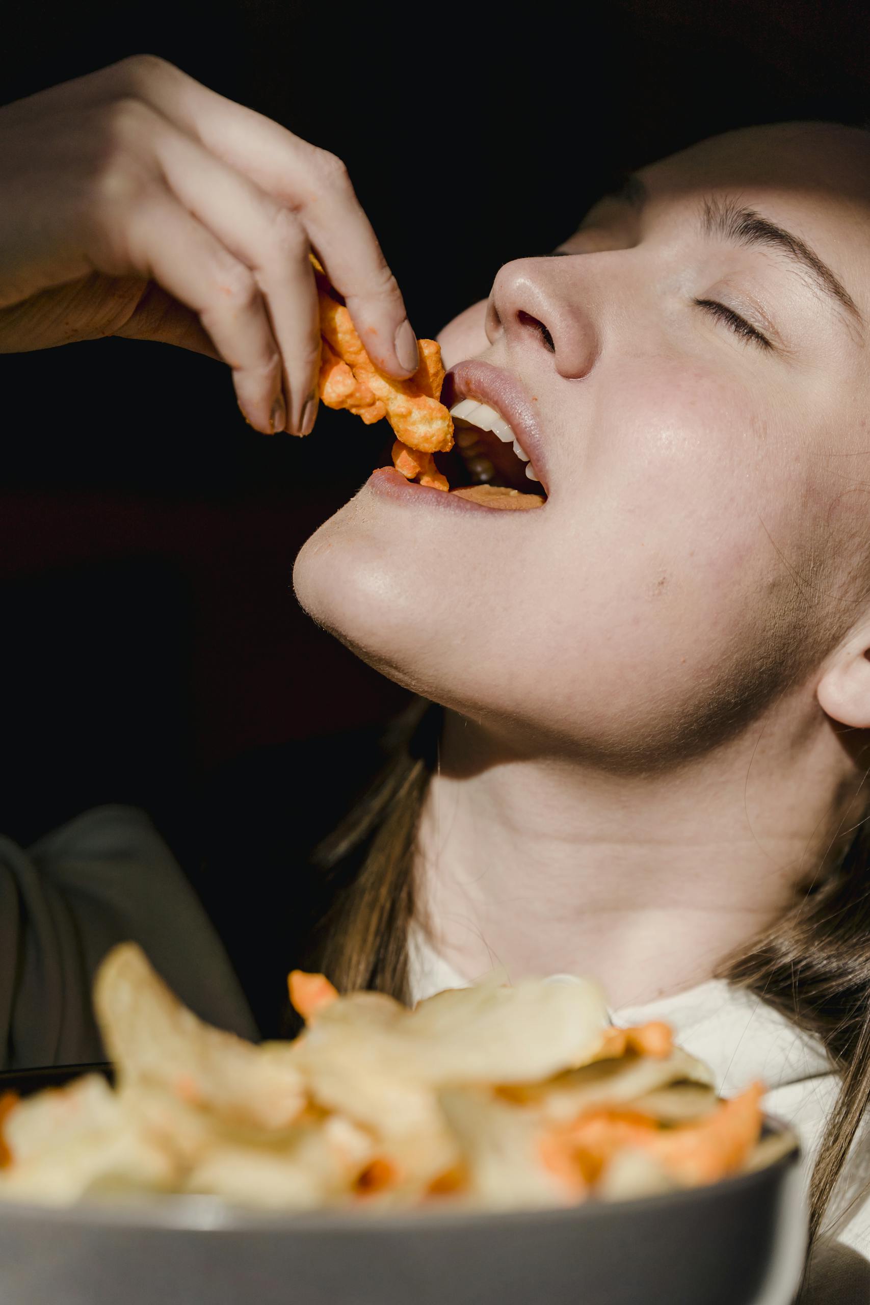 Close-up of a woman savoring delicious crunchy snacks in a bowl, showcasing enjoyment and hunger.