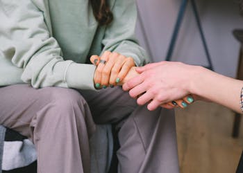 Close-up of two people holding hands during a comforting therapy session.