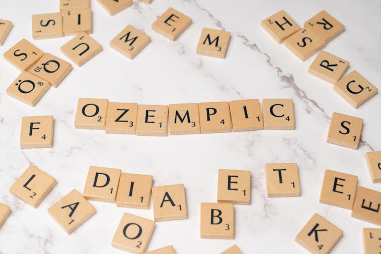 Scrabble tiles spelling Ozempic and diabetes on a marble surface.