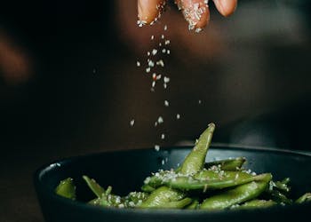 A hand sprinkles salt on fresh edamame, showcasing a delicious and healthy cooking moment.