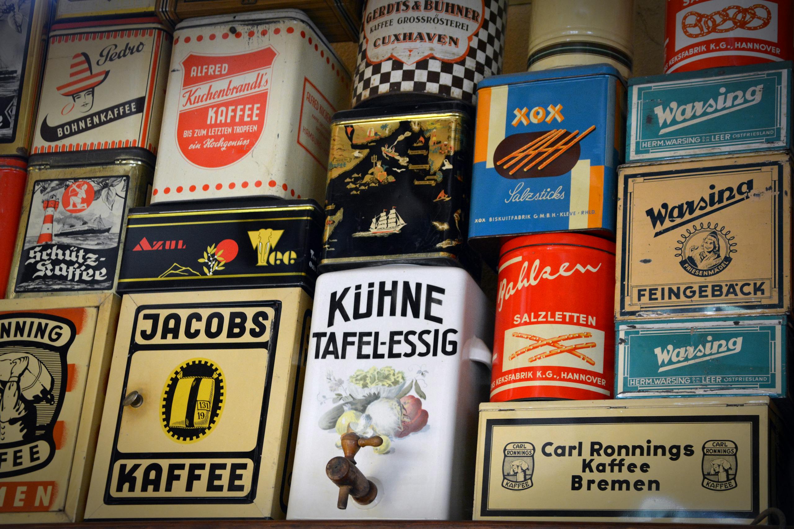 Diverse vintage German coffee tins and other containers displayed on a shelf showcasing nostalgic packaging.