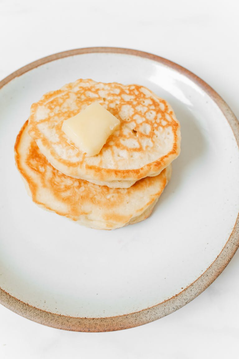 A stack of fluffy pancakes topped with melting butter on a ceramic plate, perfect for breakfast.